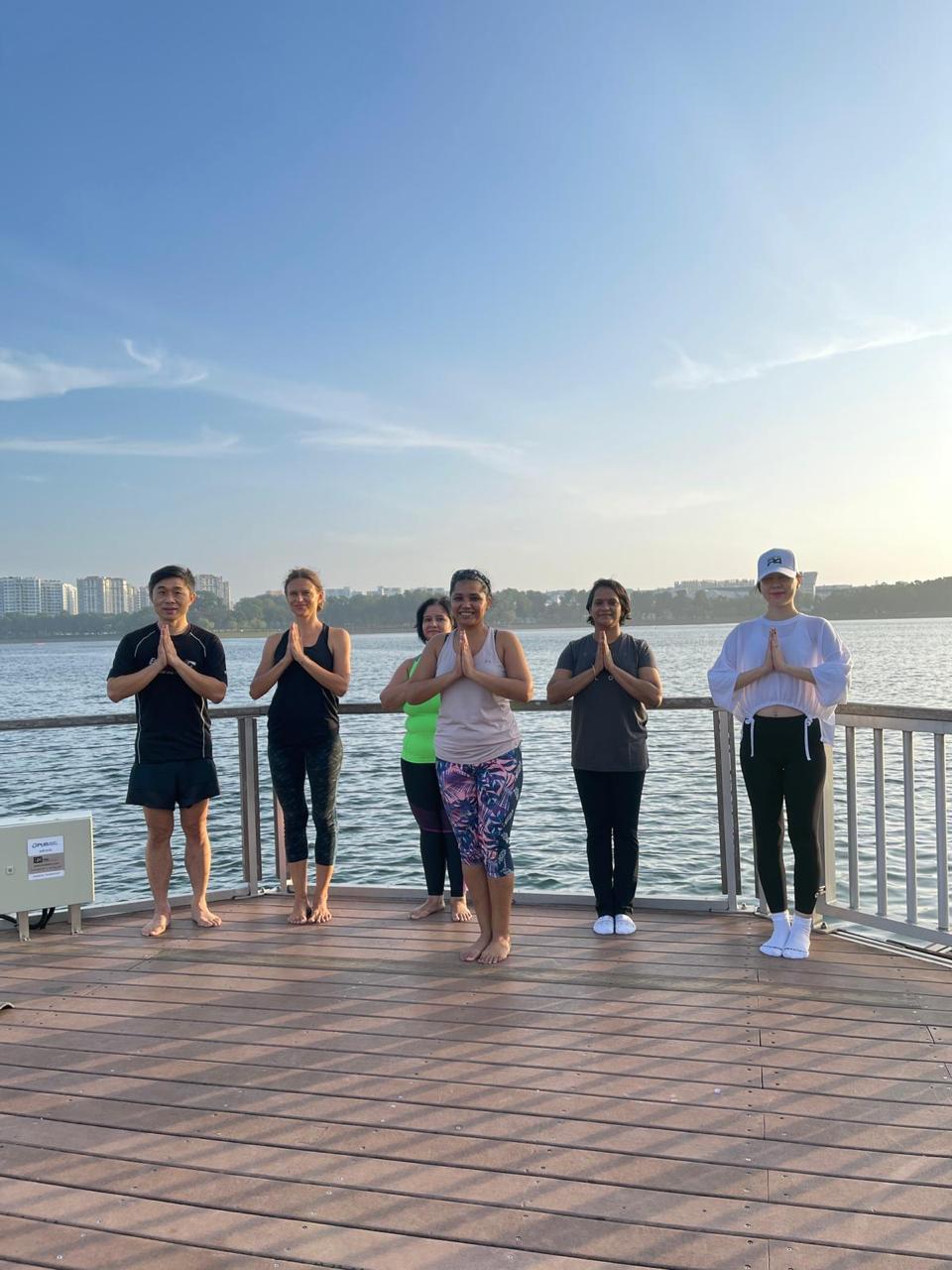 A group standing in prayer pose at sunrise on a lakeside deck