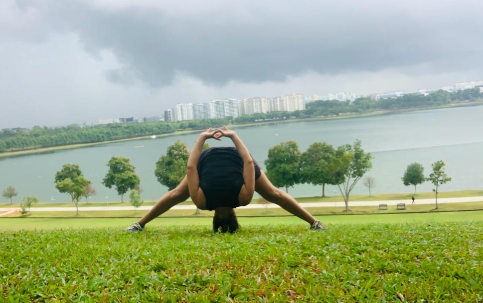 A wide-legged forward fold on the grass by a lake