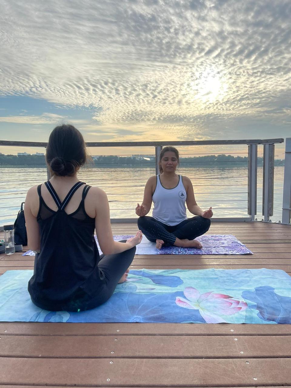 Two people in seated meditation at sunrise on a deck